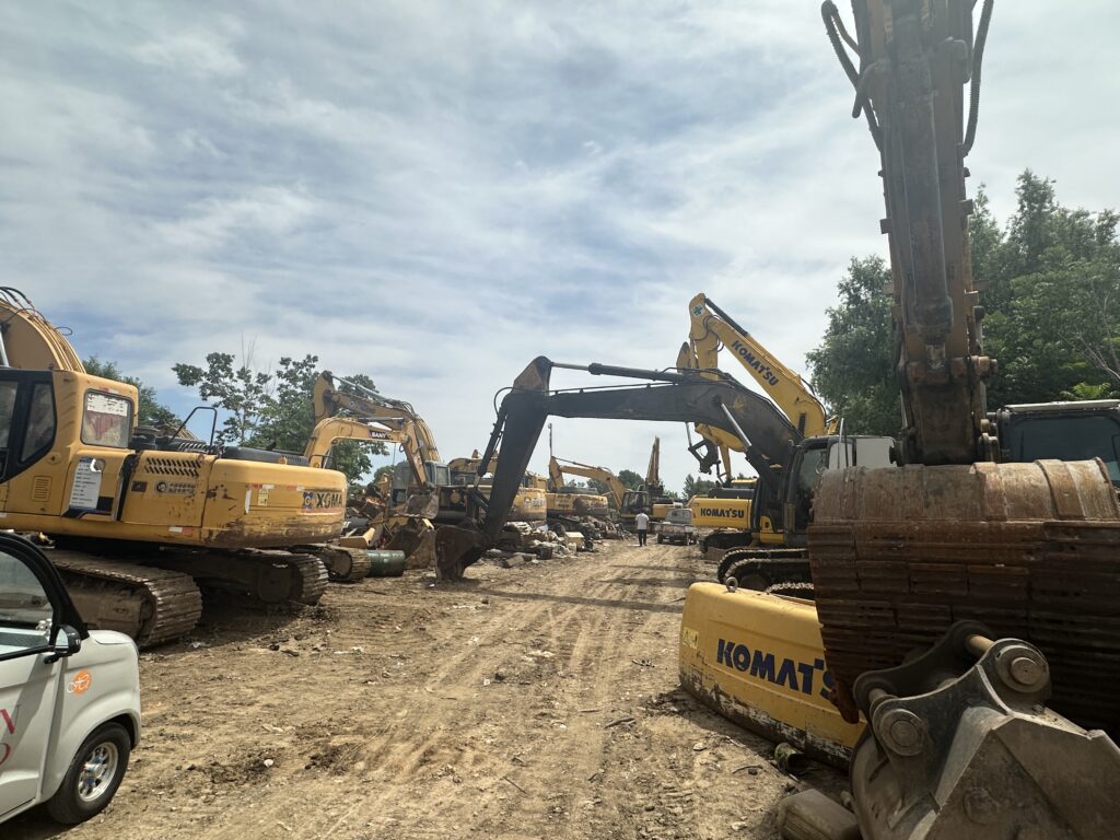 Used excavators parked along a working equipment-yard aisle
